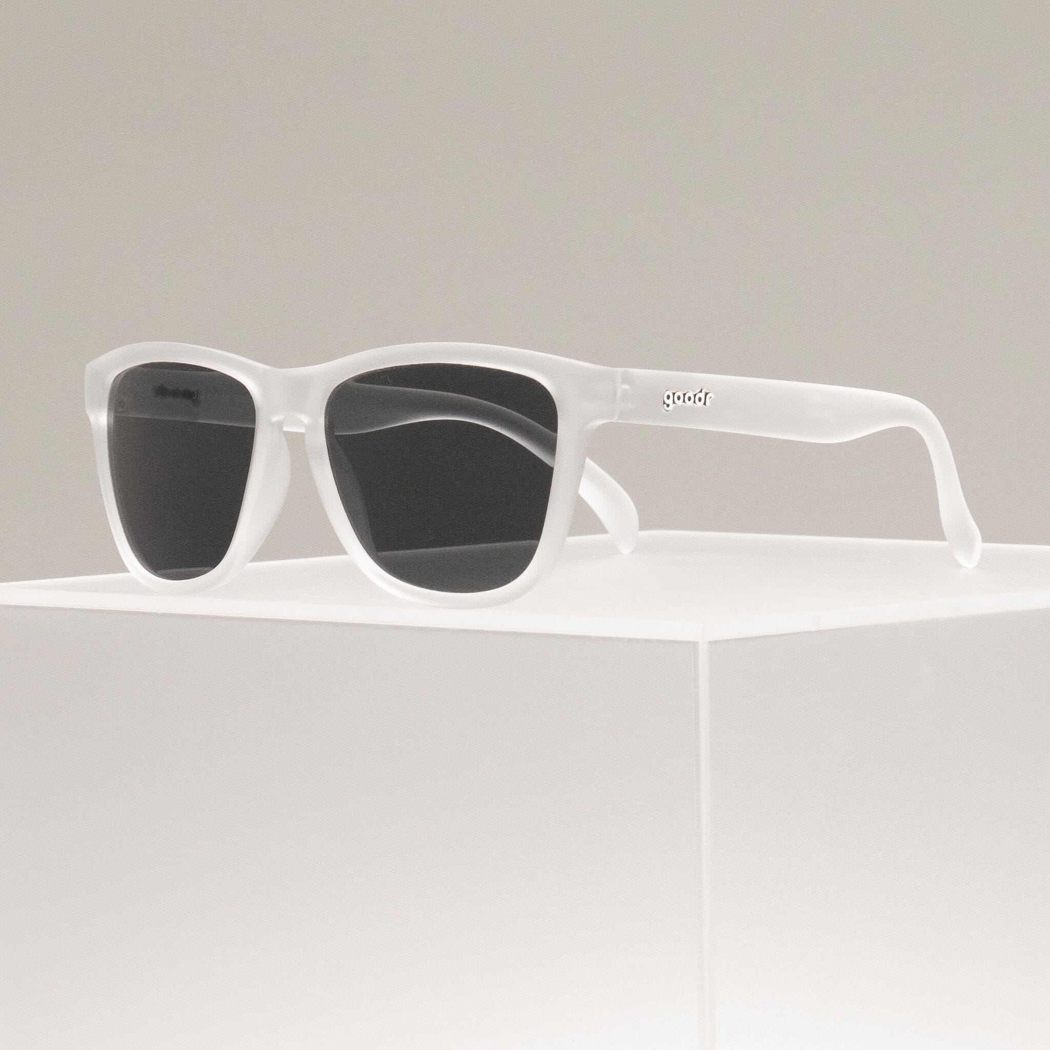 Three-quarter view of clear sunglasses with black non-reflective lenses in a classic frame shape perched atop a clear box.
