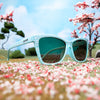 Three-quarter angle view of light blue cherry blossom sunglasses sitting in a miniature landscape of cherry blossom trees.