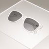 Clear sunglasses in a classic frame shape with black non-reflective lenses folded, sitting atop a clear plastic box.