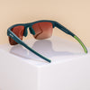 Three-quarter back angle view of solid green half-rim sunglasses with rose gradient lenses. The arms are extended, showcasing the goodr logo on the outer left arm, an adjustable silicone nose piece, and lime green silicone grips on the inner arms.
